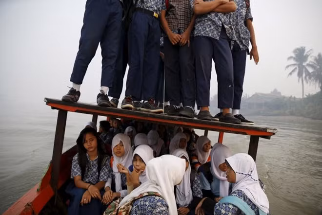 Một chiếc thuyền chở nhiều học sinh đến trường tại khu vực Palembang, đảo Sumatra, Indonesia. Chiếc thuyền quá tải khiến nhiều học sinh phải đứng trên nóc thuyền