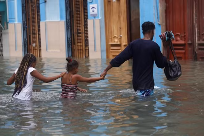 Người đàn ông dắt theo hai đứa con của mình băng qua vùng bị lụt nghiêm trọng ở thủ đô Havana, Cuba