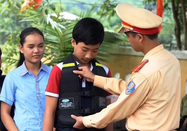 Cảnh sát Giao thông Công an Quảng Bình hướng dẫn các em học sinh xã Thuận Hóa mặc áo phao đúng cách để đảm bảo an toàn.
