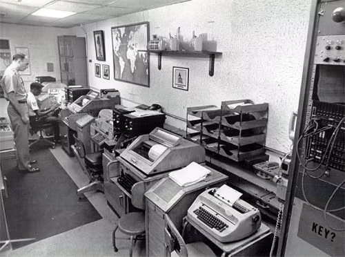 Phòng trạm cuối tại NMCC của Lầu Năm Góc trong bức ảnh năm 1976. Nơi có 2 cỗ máy teletype bảng chữ cái Latin và 2 máy bảng chữ cái Kirin, cùng 4 máy mật mã Etcrrm II. Ảnh nguồn: UPI.