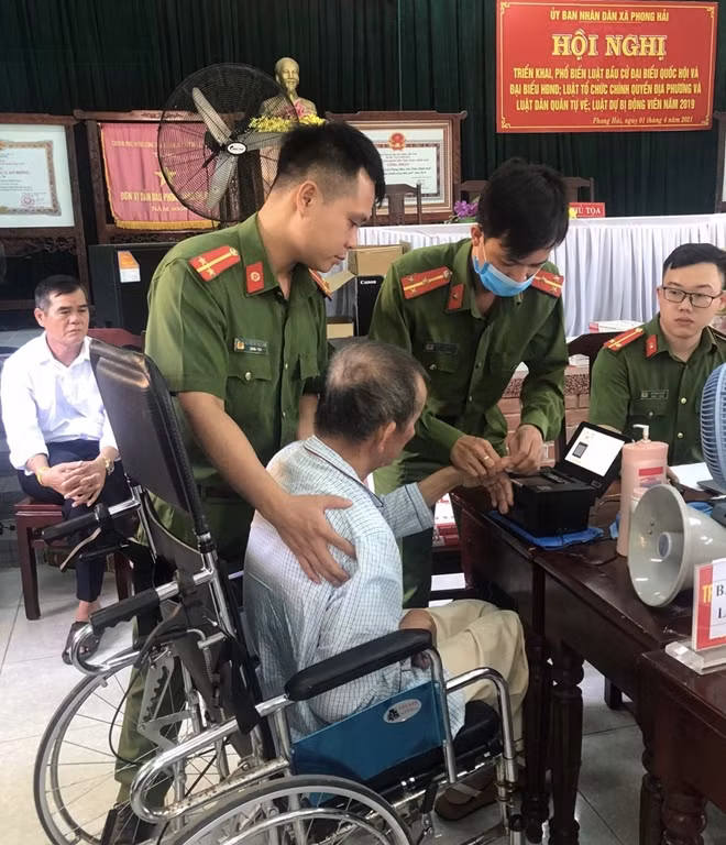 Các chiến sĩ giúp đỡ một cụ già bị bại liệt trong khi lấy vân tay.