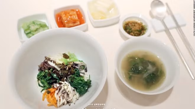 Món cơm trộn Hàn Quốc gồm rau và trứng ốp lòng đào sẽ được phục vụ trong một chiếc bát inox lớn. Gạo để nấu cơm cho món ăn này được thu hoạch tại làng Bongha, tỉnh Gimhae của cựu Tổng thống Hàn Quốc Roh Moo-hyun, người đã tới Bình Nhưỡng để tham dự hội nghị thượng đỉnh liên Triều năm 2007. Ngoài ra, phần rau xanh của món cơm trộn được trồng ngay tại vùng DMZ.