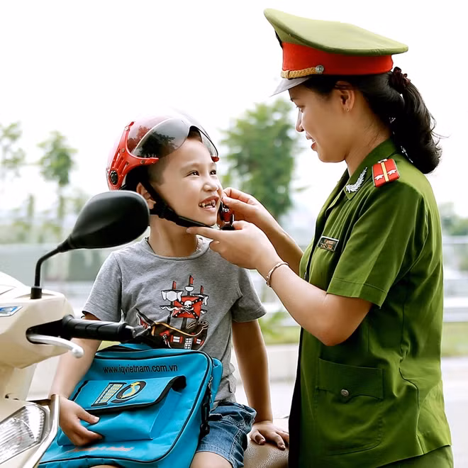 Trung úy Vũ Thị Thu Hà, Công an huyện Mê Linh, Hà Nội hướng dẫn trẻ đội mũ bảo hiểm khi tham gia giao thông. Tác giả Bình Quang.