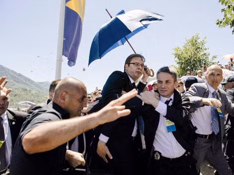 Các vệ sĩ đã phải dùng ô để che chắn cho Thủ tướng Vucic và đưa ông đi khỏi nơi tưởng niệm. Ảnh: AP.