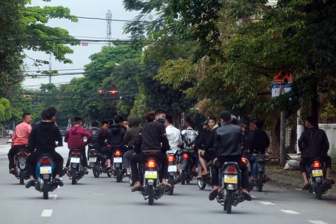 Ảnh chụp ghi lại sự việc nhóm thanh thiếu niên đi xe máy, không đội mũ bảo hiểm, dàn hàng ngang trên đường đô thị, một số xe không gắn biển số.