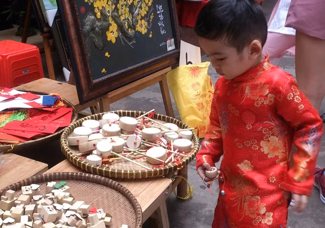 Cậu bé trong trang phục áo dài tò mò xem một gian hàng đồ chơi dân gian