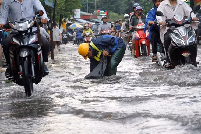 Công nhân vệ sinh móc cống kẹt rác trên đoạn đường ngập