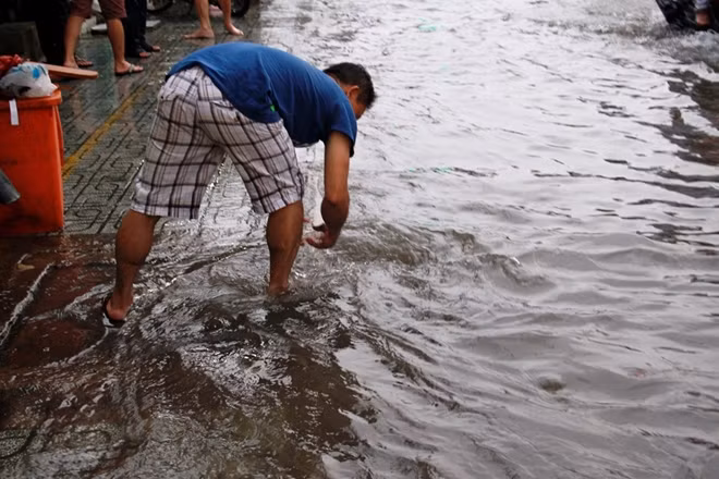 Người dân vớt rác ở miếng cống để nước thoát nhanh hơn