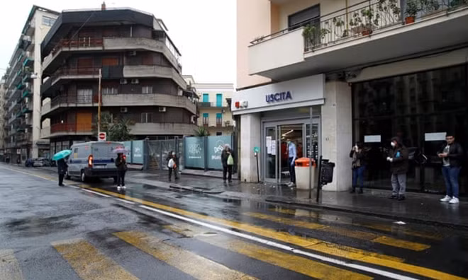 Người dân chờ đợi mua đồ bên ngoài một cửa hàng tại Sicily. Ảnh: TG