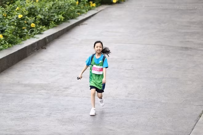 Nguyễn Quỳnh Nhi (Bib 1067) sinh năm 2011, nở nụ cười tươi trên đường đua. Em dù khá mệt nhưng đang cố gắng về đích với mục tiêu thời gian đã đề ra.