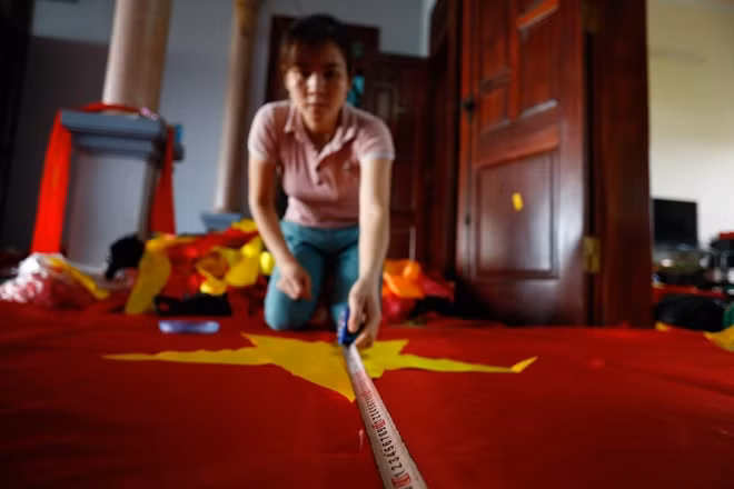 Chị Duyên, vợ anh Phục đo kích thước ngôi sao để cân bằng. Chị cũng là một thợ làm cờ lành nghề, ngay từ bé chị đã biết thêu thùa nên khi về làm dâu, chị học nghề rất nhanh.