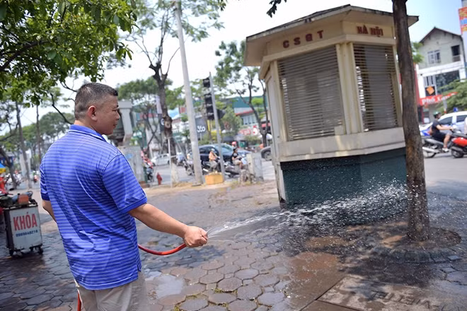 Để giảm bớt nhiệt nắng nóng, người đàn ông này phun nước ra vỉa hè phía trước cửa nhà.