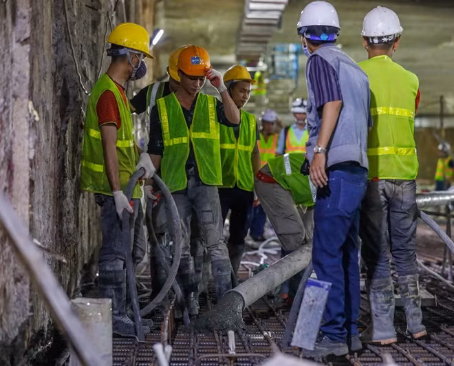 Nhiều công nhân hỗ trợ lắp đặt và điều khiển ống phun bê tông tươi.