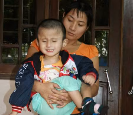 Chị Vịnh bế bé Đức đứng trước ngôi nhà anh chị ở nhờ.