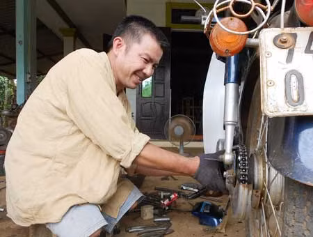 Ông Nguyễn Văn Sự (bị cụt hai chân) đang sửa xe máy tại quán của mình.