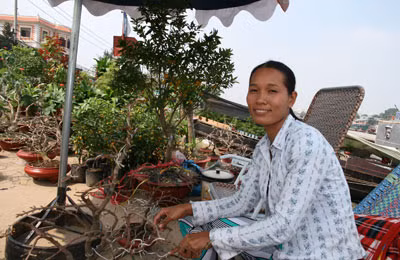 Anh Phạm Văn Hạnh đang chăm sóc những cây mai kiểng của mình. Chị Võ Thị Út bên quầy hoa kiểng.