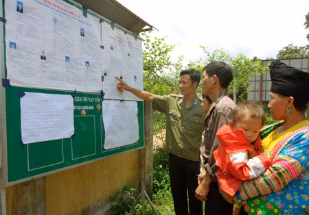 Cán bộ Công an hướng dẫn bà con về bầu cử tại điểm niêm yết danh sách ứng viên ở xã Nậm Kè, Mường Nhé.