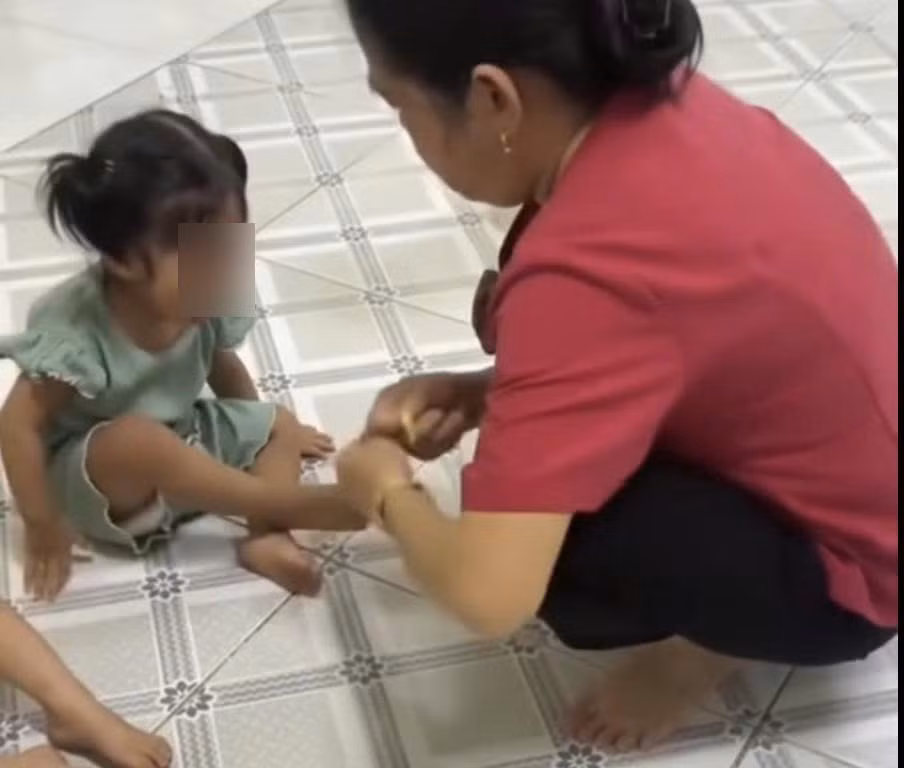 Nữ giáo viên dùng dây thun tác động vào chân trẻ. (Ảnh cắt từ clip).