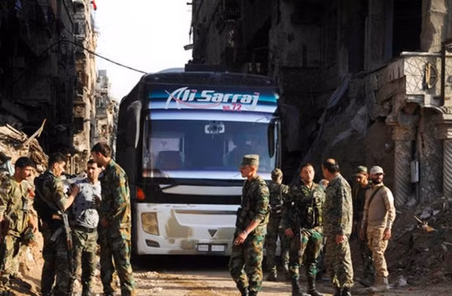 Các binh sĩ Syria đứng cạnh xe bus dành cho hoạt động sơ tán của phiến quân. Ảnh: ITN