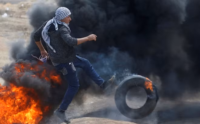 Một thanh niên Palestine đá lốp vào đám cháy trong cuộc biểu tình hôm 14-5. Ảnh: Reuters