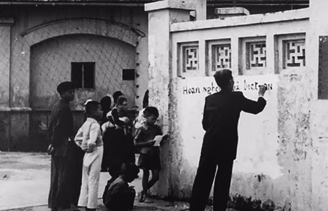 Trong rừng cờ hoa với niềm vui hân hoan, hai mươi vạn nhân dân Thủ đô náo nức đón đoàn quân chiến thắng, sau 9 năm kháng chiến trường kỳ. Trong ảnh là người dân kẻ khẩu hiệu chào mừng lên tường trường Trần Nhật Duật, tháng 10-1954.