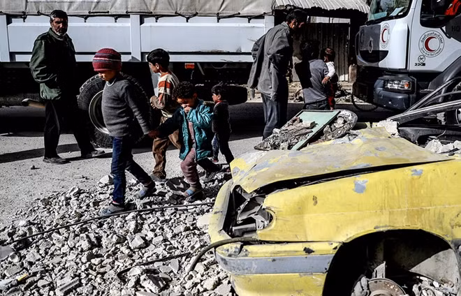 Các em nhỏ ở Đông Ghouta chơi đùa bên cạnh đoàn xe nhân đạo. Ảnh: EPA