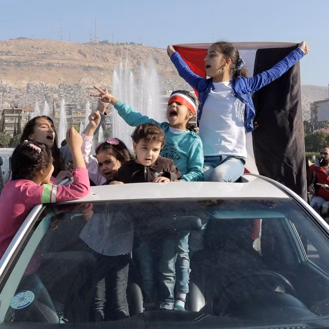 Các em nhỏ Syria cầm quốc kỳ chơi đùa trên nóc một chiếc ô tô ở thủ đô Damacus. Đòn tấn công vào rạng sáng 14-4 đánh dấu lần thứ hai Tổng thống Mỹ Donald Trump ra lệnh không kích Syria với cáo buộc Damacus sử dụng vũ khí hoá học nhằm vào thường dân.