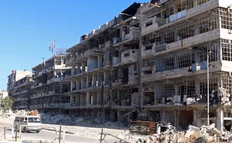 Một chiếc xe buýt đi qua tòa nhà đổ nát dọc một con phố ở Al-Shaar, Aleppo, Syria, ngày 13/7. (Ảnh: Reuters).