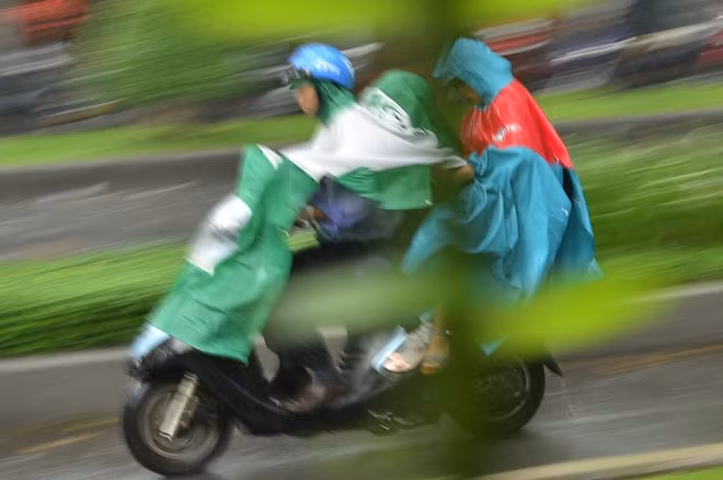 Hình ảnh 2 vợ chồng đi đón con trong giờ tan trường che kín áo mưa.