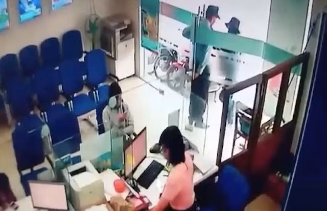 Bảo vệ đứng chắn trước cửa kính của phòng giao dịch khi tên cướp bước vào.
