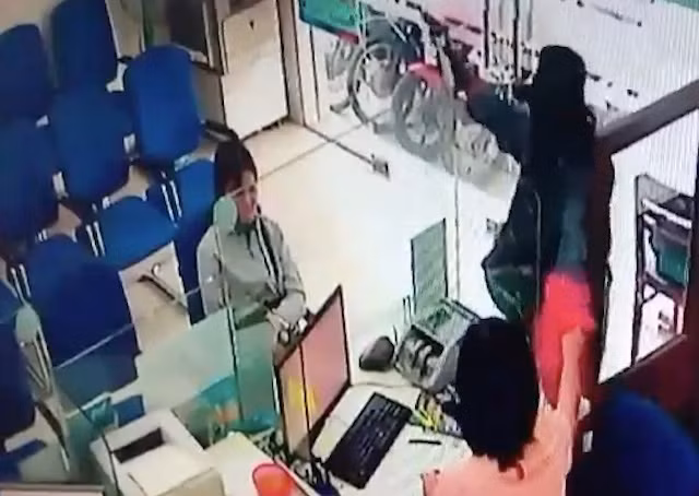 Nữ nhân viên gom tiền cho vào túi màu hồng, đưa cho tên cướp.