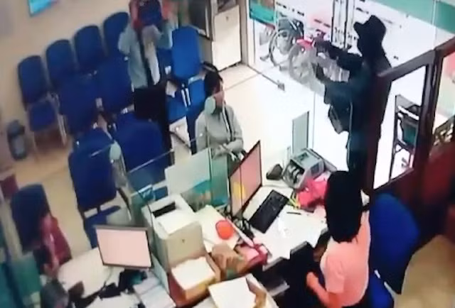 Tên cướp liên tục chĩa vật giống khẩu súng, đe dọa những người có mặt tại phòng giao dịch.
