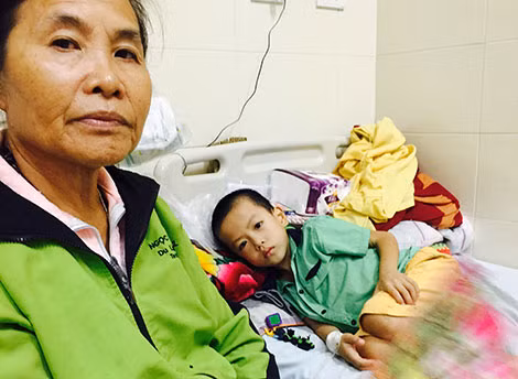 Bé Nguyễn Đình Dũng nằm đau đớn trên giường, bên cạnh là bà nội. Bé Nguyễn Đình Dũng nằm đau đớn trên giường, bên cạnh là bà nội.