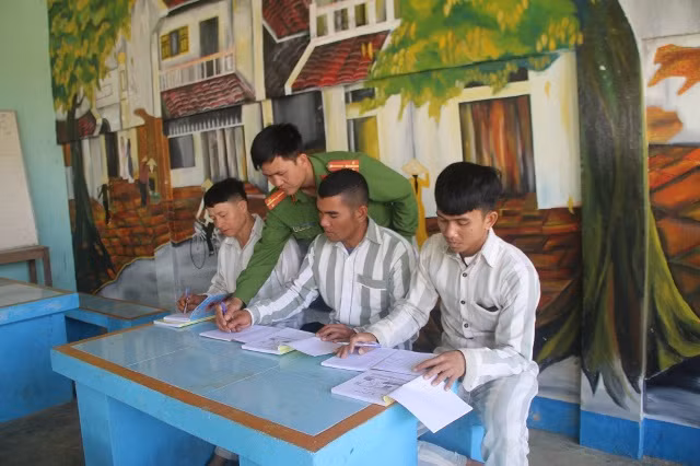 Cán bộ giáo dục cầm tay, hướng dẫn các phạm nhân viết chữ.