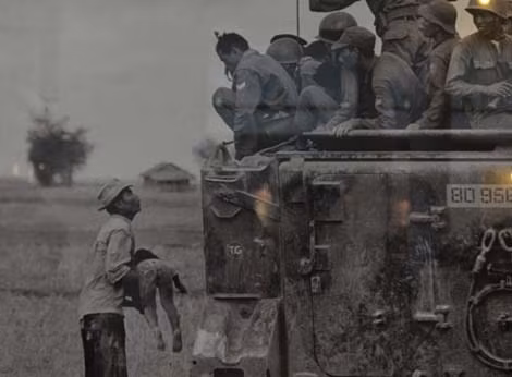 Một người cha đau đớn ôm thi hài con khi lính biệt kích Việt Nam Cộng hòa ngồi trên xe bọc thép nhìn xuống. Ảnh của Horst Faas- giải Pulitzer năm 1965.