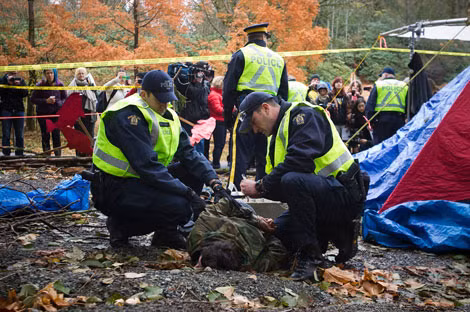 Nhân viên RCMP bắt giữ một nhà hoạt động trong cuộc biểu tình chống dự án đường ống dẫn dầu ở British Columbia, ngày 20/11/2014. Nhân viên RCMP bắt giữ một nhà hoạt động trong cuộc biểu tình chống dự án đường ống dẫn dầu ở British Columbia, ngày 20/11/2014.