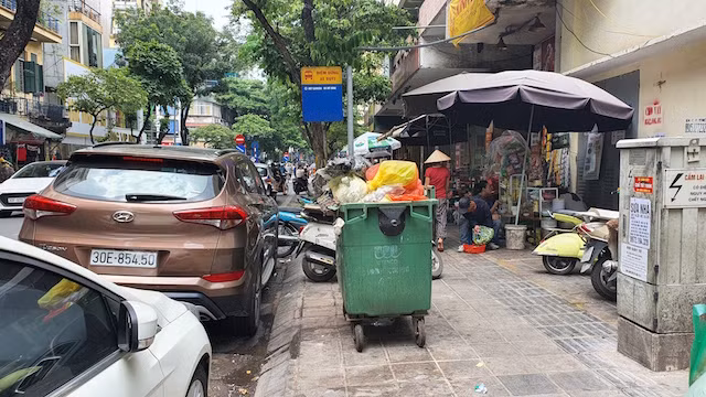 Điểm dừng xe buýt tại cửa chợ Hôm, phố Trần Xuân Soạn, bị vây kín bởi xe rác và xe dừng đỗ sai quy định.