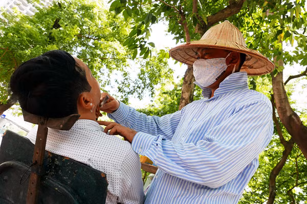 Người thợ cắt tóc "vỉa hè" gần ngã tư Thái Hà - Chùa Bộc phải đội mũ chống nắng nóng trong lúc làm việc.