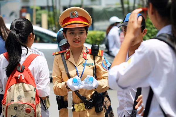 Nhiều cảnh sát giao thông vẫn phải làm việc dưới nắng nóng. Trong ảnh là nữ cảnh sát thuộc Đội cảnh sát giao thông số 3, Công an Hà Nội, vừa làm nhiệm vụ điều tiết giao thông giữa trưa nắng vừa phát nước miễn phí cho các thí sinh thi THPT quốc gia tại điểm thi Đại học Thủy Lợi.