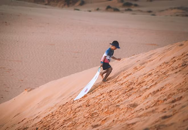 Đứa trẻ cho thuê ván trượt trên đồi cát.