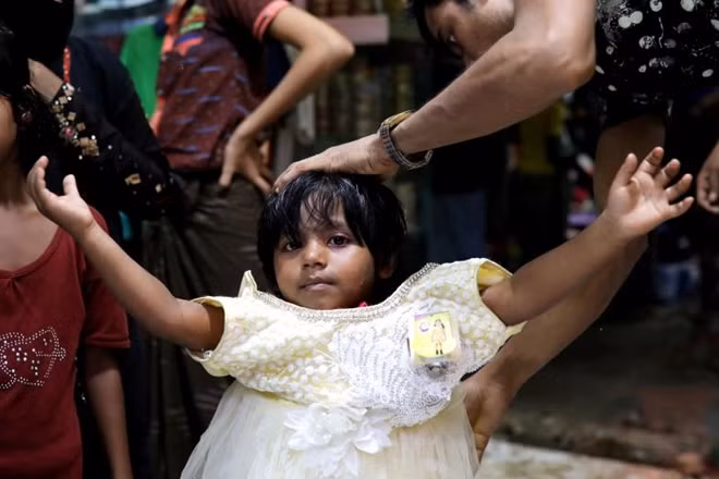 Một em bé người Rohingya đang thử một chiếc váy mới tại một cửa hàng trong khu trại tị nạn Kutupalong ở Cox's Bazar, Bangladesh.