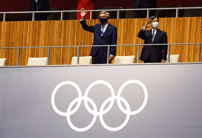Chủ tịch Ủy ban Olympic Quốc tế (IOC) Thomas Bach (trái) và Nhật hoàng Naruhito (phải) gửi lời chào từ khán đài, sau đó cả hai người đều ngồi cách xa nhau để đảm bảo giãn cách. (Ảnh: Reuters)