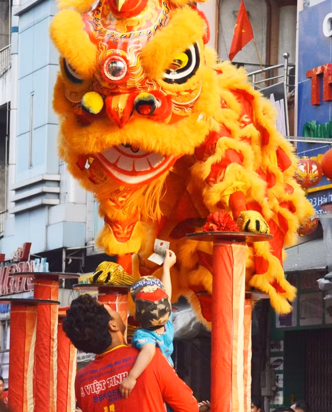 Một em bé được bế lên để đưa tiền cho lân ăn trên đường Hải Thượng Lãn Ông