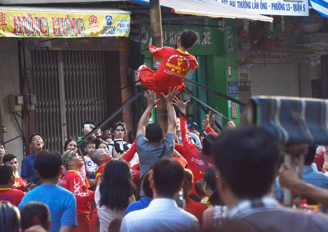 Một người biểu diễn múa lân trên cây sào cao hàng chục mét được người trong đoàn đỡ khi biểu diễn xong