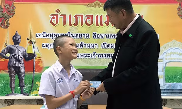 Thành viên đội bóng "Lợn hoang" cười rạng rỡ khi được cầm tấm thẻ căn cước công dân trên tay. Ảnh: The Guardian