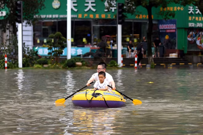 Người đàn ông đang dùng xuồng cá nhân để đưa một cậu bé ra khỏi khu vực ngập úng tại Chiết Giang hôm 10-8. Ảnh: Reuters