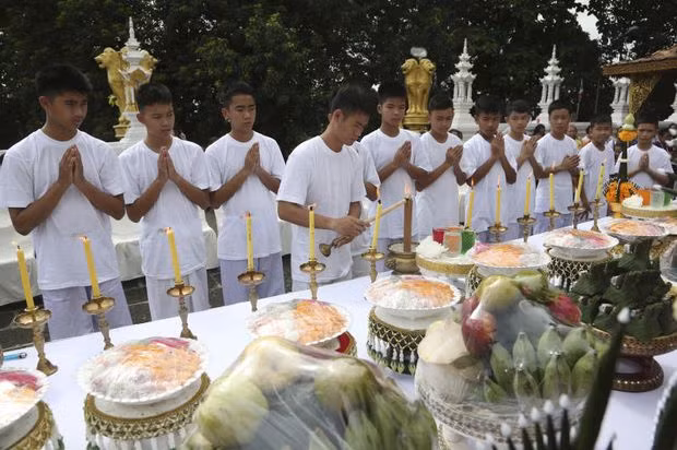 Các thành viên đội bóng trong trang phục trắng đang thắp những ngọn nến vàng để gửi lời cảm ơn và tri ân. Ảnh: AP