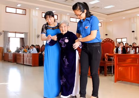 Tình nguyện viên địa phương dìu mẹ lên nhận danh hiệu.