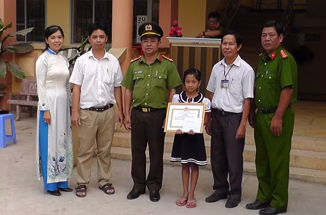 Lãnh đạo Công an huyện và Hiệu trưởng nhà trường trao khen cho em Nam và Lợi.