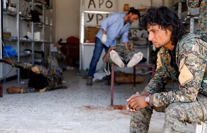 Một tay súng của Lực lượng Dân chủ Syria ngồi chờ trong lúc đồng đội đang được nhân viên y tế cứu chữa sau khi bị thương do IS bắn tỉa hồi 28-6.